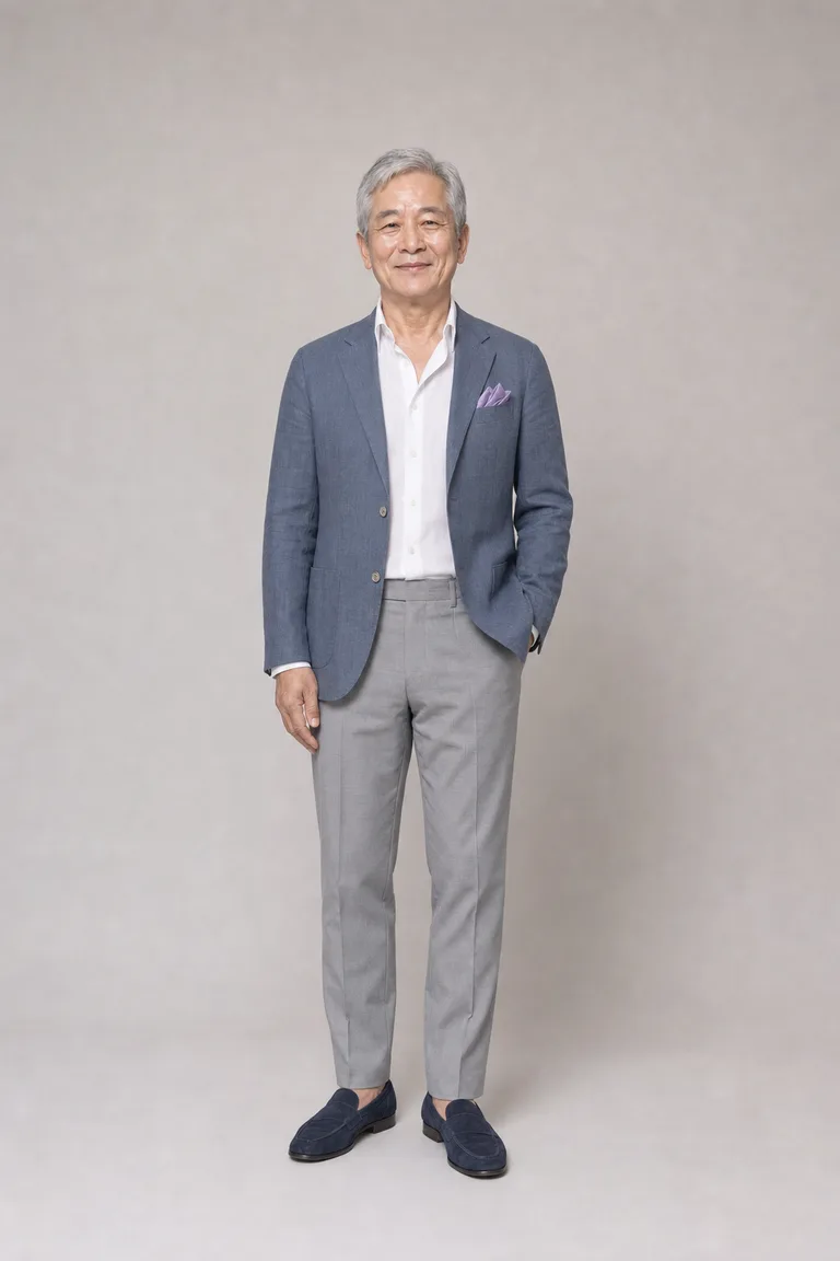Man in his sixties wearing a slate blue linen blazer, white linen shirt, light gray trousers and navy suede loafers.
