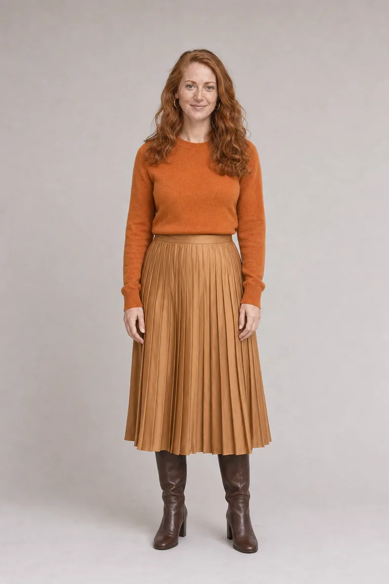 A woman with copper-red hair in a pumpkin cashmere sweater, camel pleated midi skirt and chocolate knee-high boots.